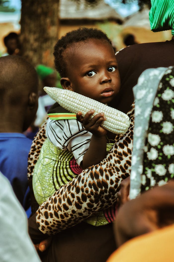 A child holds corn in a colorful outdoor setting in Nalerigu, Ghana.